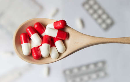 Red and white capsules in a wooden spoon on blurred background of pills, tablets, capsules. Top view.の写真素材