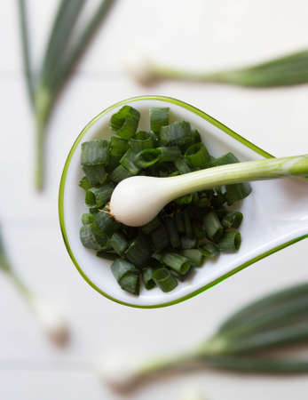Chopped fresh green onions in spoon on blurred background of whole onions. Top view.