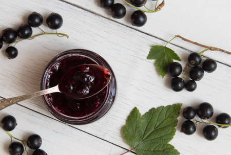 Currant homemade jam in glass jar on the white wooden table decorated with black currant and green leaves.の写真素材
