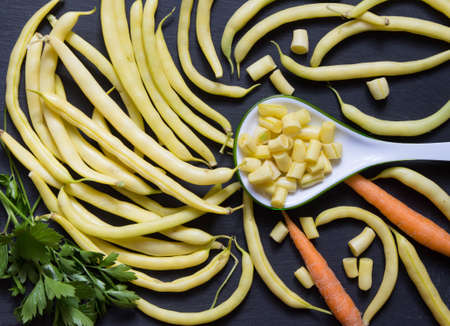 Freshly harvested yellow runner beans and spoon with chopped beans on stone. Top view, ingredient...