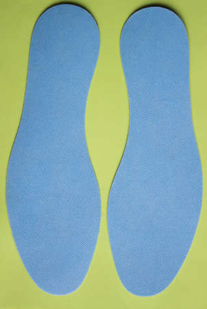 Pair of blue insoles for shoes on yellow background. top view.