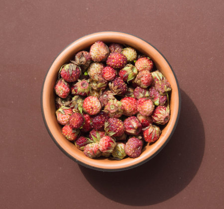 Fresh ripe red berries of wild forest strawberries in brown bowl. top view. Meadow strawberries on brown background.の写真素材