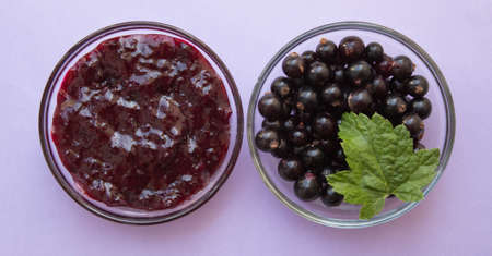 Berries fresh black currant and homemade jam in bowl. Violet background. Summer menu, natural vitamins. top view.の写真素材