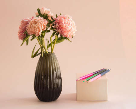 Bouquet of asters flowers in vase and colored pencils on a box. Pink garden flowers on pastel background.の写真素材