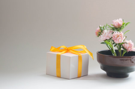 Fresh pink flowers in vase with gift box and yellow ribbon. Romantic floral arrangement, neutral background.の写真素材