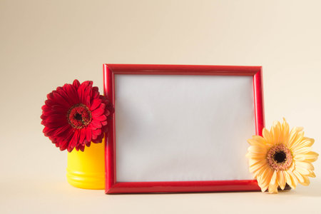 Empty photo frame with red and yellow gerbera daisy flowers on pastel beige background. Picture frame mockup with flowers, Copy space.の写真素材