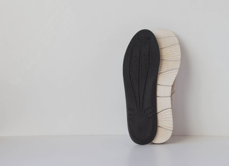 The black insole and sole of the sports shoe are positioned vertically. Light background. Foot care products conception.の写真素材