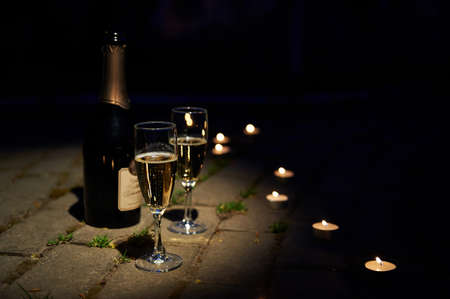Bottle of champagne with two glass goblets on a thin stalk and romantic candles