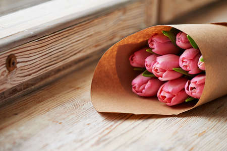a bouquet of tulips wrapped in paper on old wooden backgroundの写真素材