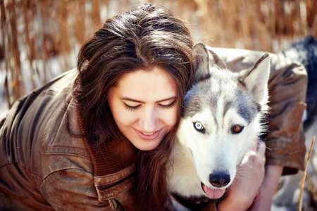 Beautiful woman with husky outdoors.Happy brunette woman with smiling siberian husky dog, sitting in a poppy field on a sunny day, on a walk with dogの写真素材