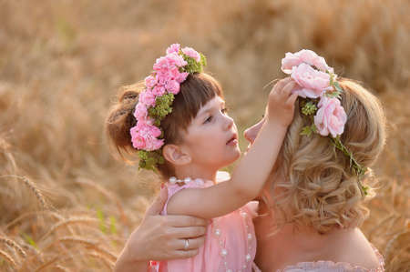 The daughter and mother look at each other, the daughter straightens the wreath of roses on her headの写真素材