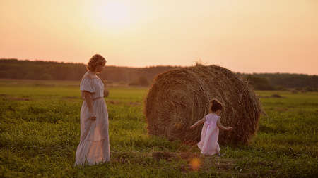 mother and daughter run on the field. Long dresses. The haystackの写真素材