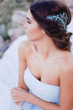 Gorgeous young brunette European type sits in profile on the beach, looking romantically into the distance. Beautiful hair decoration handmadeの写真素材