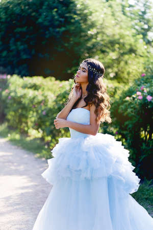 Gorgeous brunette in a lush blue dress with her hair is set in a lush gardenの写真素材