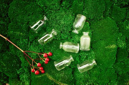 Lot of small glass vials lying on the lush moss and next to a branch of red berries of Hypericumの写真素材