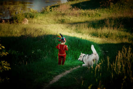 a little boy in a red suit Indian plays with a dog husky runs on the field and trailsの写真素材