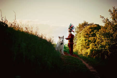a little boy in a red suit Indian plays with a dog husky runs on the field and trailsの写真素材