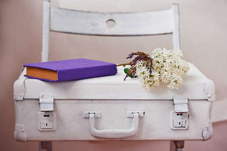 White painted suitcase on a light background, with the lilac and purple book.の写真素材