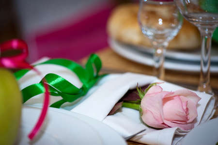 A wedding decoration. Devices with a pink rose in a linen napkin on a wedding tableの写真素材