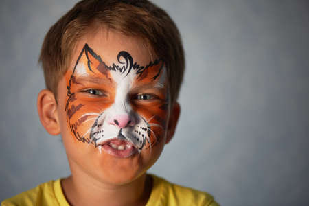 6 years old boy with blue eyes with face painting of a cat or a tiger. Orange.の写真素材