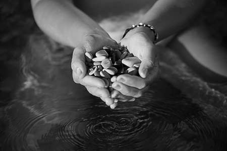 Black and white image of clasped hands with the sea stones on the background of water, the falling dropsの写真素材