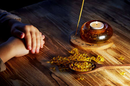 The hands of the child, cod liver oil on a wooden spoon and on a wooden surface is scattered. The...