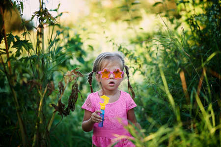 The girl in the pink dress 3 years and two braids enjoys life, inflating bubbles.の写真素材