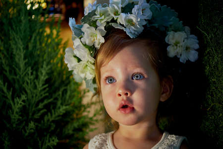 Beautiful little girl in a wreath on the head in green and white. Party dress, little Princess.の写真素材
