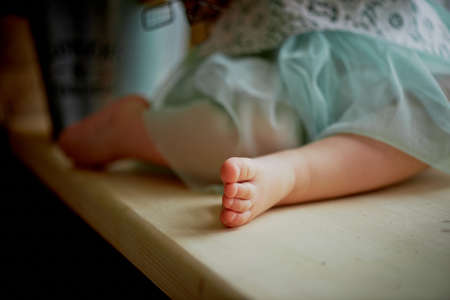 The legs of the baby sitting on the windowsill in turquoise skirtの写真素材