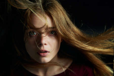 Beautiful girl looks piercing eyes into the camera. Hair flying. Drama. Studio photography in low key on a backgroundの写真素材