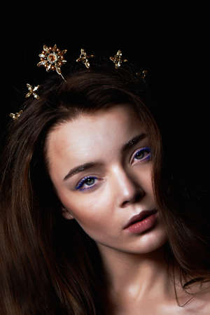 Portrait of a gorgeous girl with a decoration on the head in the shape of a crown. Long hair. In a Studio on a dark backgroundの写真素材