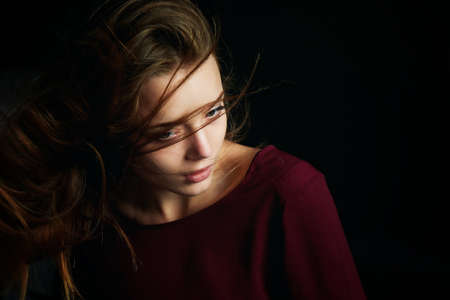 Beautiful girl looking to the side, in profile, Hair flying. Drama. Studio photography in low key on a backgroundの写真素材