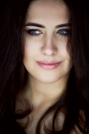 Close-up portrait of beautiful elegant brunette with long hair. In the eyes of the reflection of the lamp.Studio, dark backgroundの写真素材