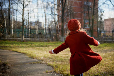 Baby 3 years with long hair. In a red beret and coat spinning in the street , in the rays of the sun. The state of happiness. Childhoodの写真素材