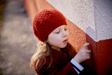 Baby 3 years with long hair. In a red beret and coat outside in the sun. Picking his . Childhoodの写真素材