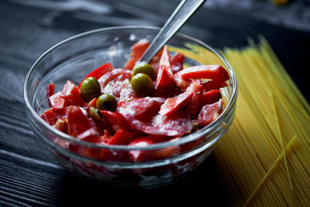 Transparent plate with a salad of tomatoes, red peppers and olives,dressed with sour cream on a dark background.の写真素材