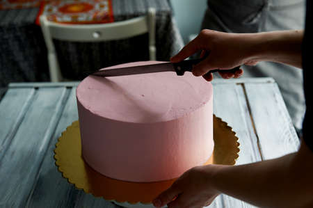 The pastry chef cut the cake with a long knife. Hands care. Cut a pink cake in a minimalist style...