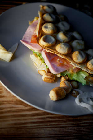 Rich Hong Kong waffle with cheese, ham, lettuce, tomato. On dark wooden background.Scattered nuts and dried squidの写真素材