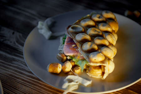 Rich Hong Kong waffle with cheese, ham, lettuce, tomato. On dark wooden background.Scattered nuts and dried squidの写真素材