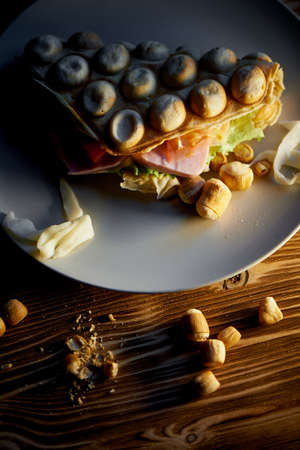 Rich Hong Kong waffle with cheese, ham, lettuce, tomato. On dark wooden background.Scattered nuts and dried squidの写真素材