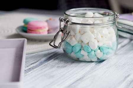 marshmallows in white and blue pastel colours on a light wooden surface. In a glass jar with a hinged lidの写真素材
