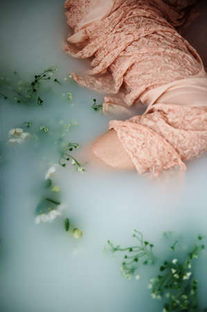 Beautiful romantic red-haired girl sitting in the bath and holding flowers .The face is not visible. In lace dress powdery pastel cream colorの写真素材