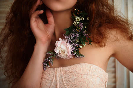 Beautiful romantic red-haired girl sitting in the bath and holding flowers .part of the face is not visible. In lace dress powdery pastel cream colorの写真素材