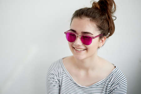 The girl smiles happily in the pink glasses. A naive view of the world in the transition to adulthoodの写真素材