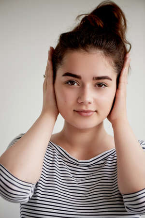 Emotions. Close-up facial portrait. Hear no evil. Girl on a light background covers his earsの写真素材