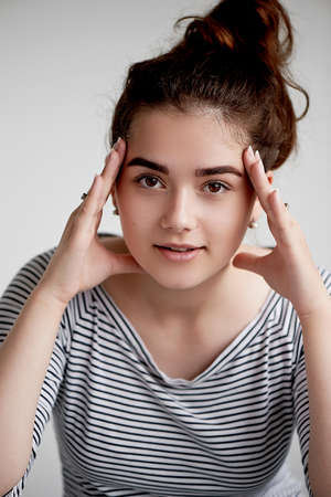 a young girl looks open confident look. Two hands of a person. About something trying. Brunette on a white backgroundの写真素材