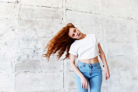 Model tests.Beautiful redhead girl with curly hair. Natural color. Dancing and moving on the background of light brick wall. Dynamicsの写真素材