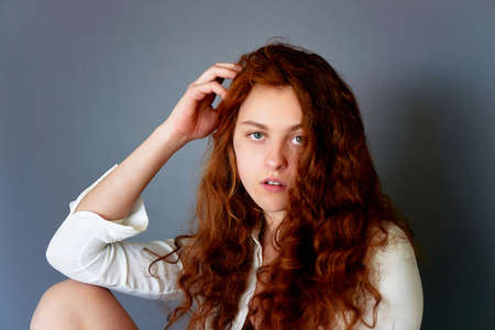 Model tests. Beautiful redhead girl with curly hair. Natural color. portrait on a grey background. Studioの写真素材