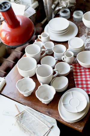 The workplace of ceramist. Baked dishes, ready for painting. A window table with a red lampの写真素材