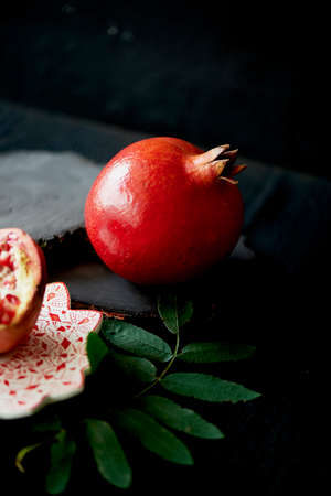 Useful antioxidant pomegranate, lies with the dark countertops. One in broken with juicy flesh. Framed by green leaves. Healthy eating during the vitamin deficiencyの写真素材